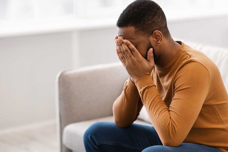 Male Depression. Desperate Depressed African Man Covering Face Crying Having Problems Sitting On Couch At Home. Emotional Stress And Unhappiness Concept. Despair, Grief And Negative Emotions