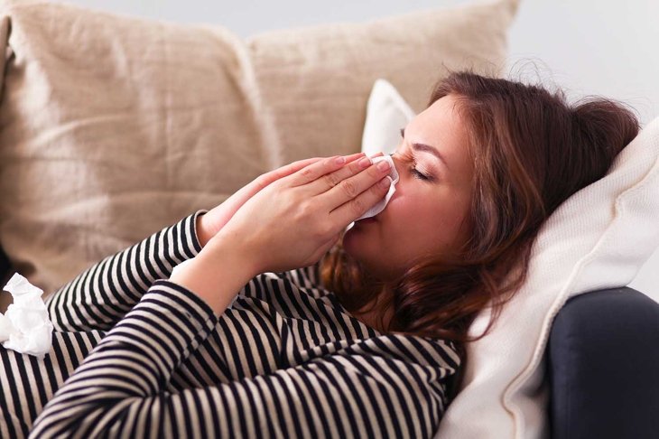 Portrait of a sick woman blowing her nose while sitting on the sofa