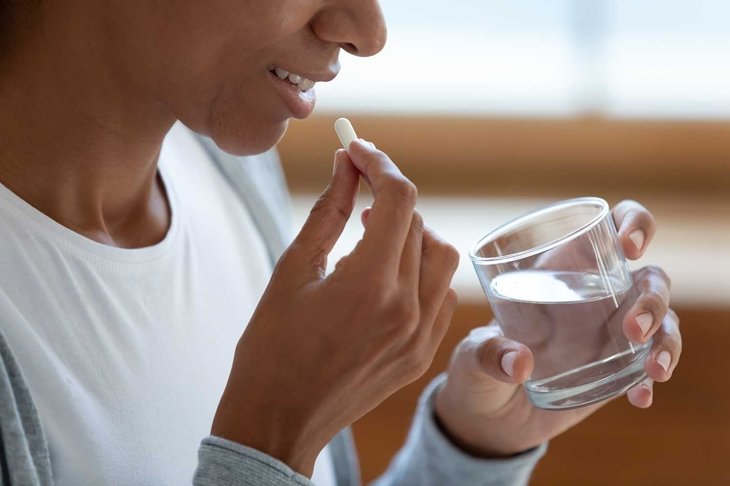 Crop close up of smiling young African American woman take daily dose of vitamin or dietary supplements. Millennial biracial female have medicines or pills drugs at home. Healthcare concept.