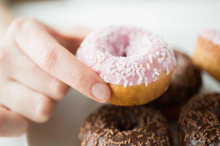 people, food, junk-food and eating concept - close up of female hand holding glazed donut