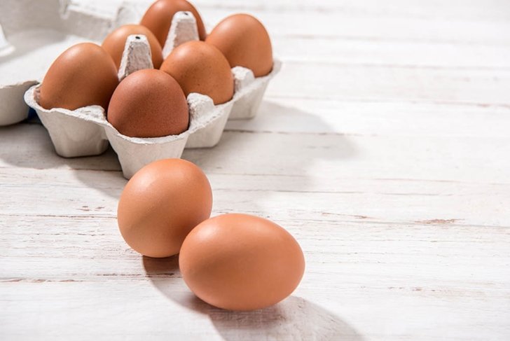 Close-up view of raw chicken eggs in egg box on white wooden background