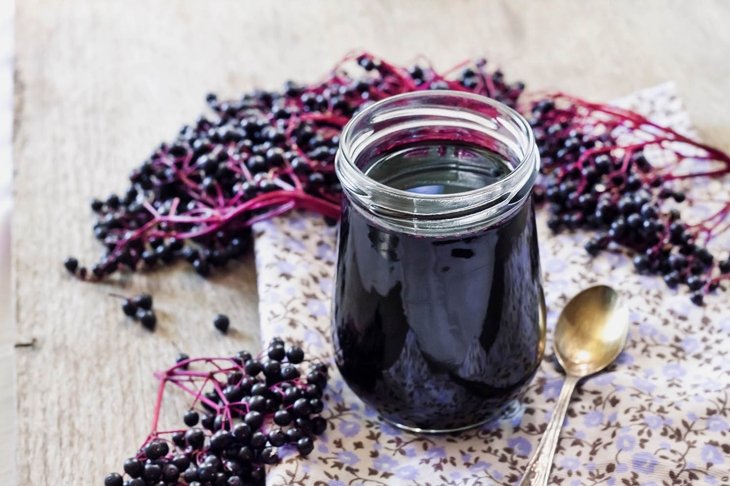 Homemade black elderberry syrup in glass jar and bunches of black elderberry in background